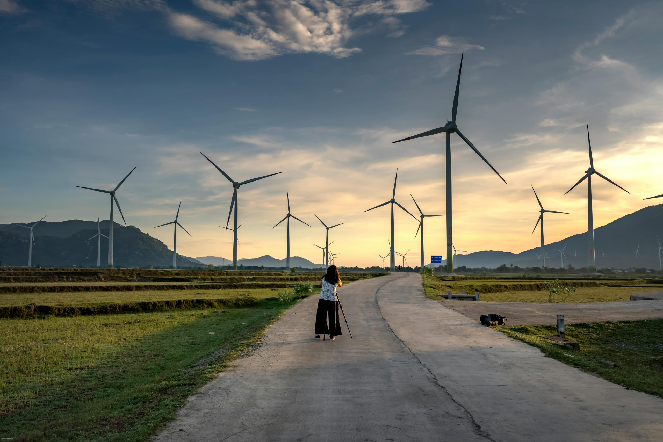 A scenic view of a wind farm at sunrise, featuring a photographer capturing the scene.